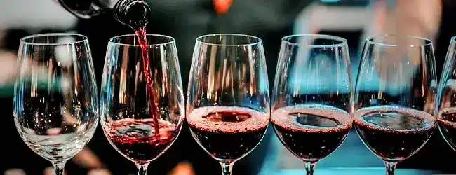 Un bicchiere di vino rosso e due bicchieri vuoti sono disposti su una superficie scura.
