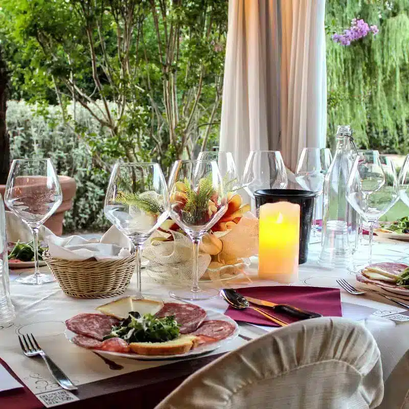 Tavolo apparecchiato in giardino con i calici, la candela e un piatto di salumi e formaggi.
