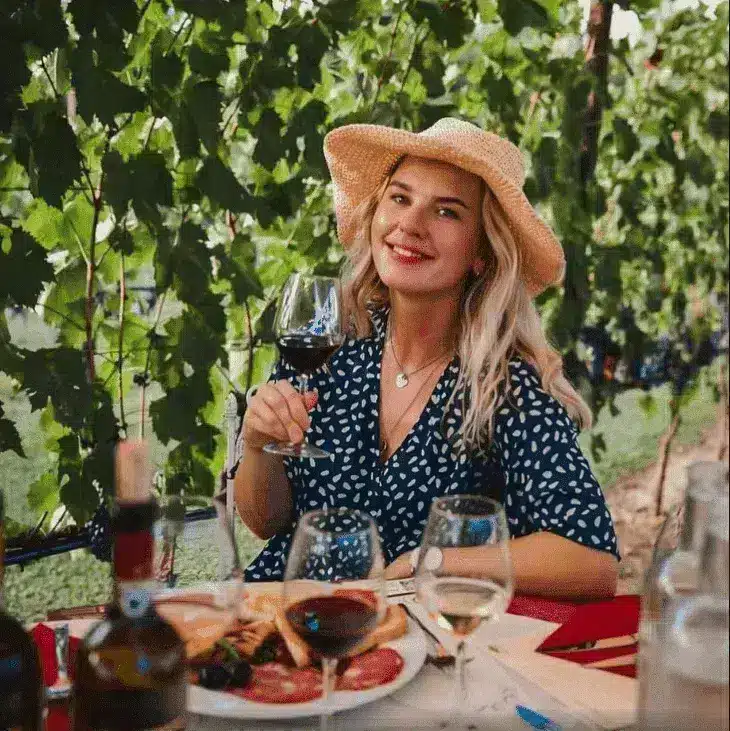 Una donna con il cappello di paglia assaggia un calice di vino rosso sotto il pergolato.
